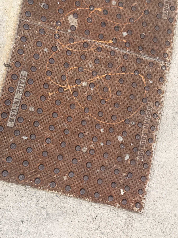 A weathered utility plate set into a sidewalk near Findlay Market.