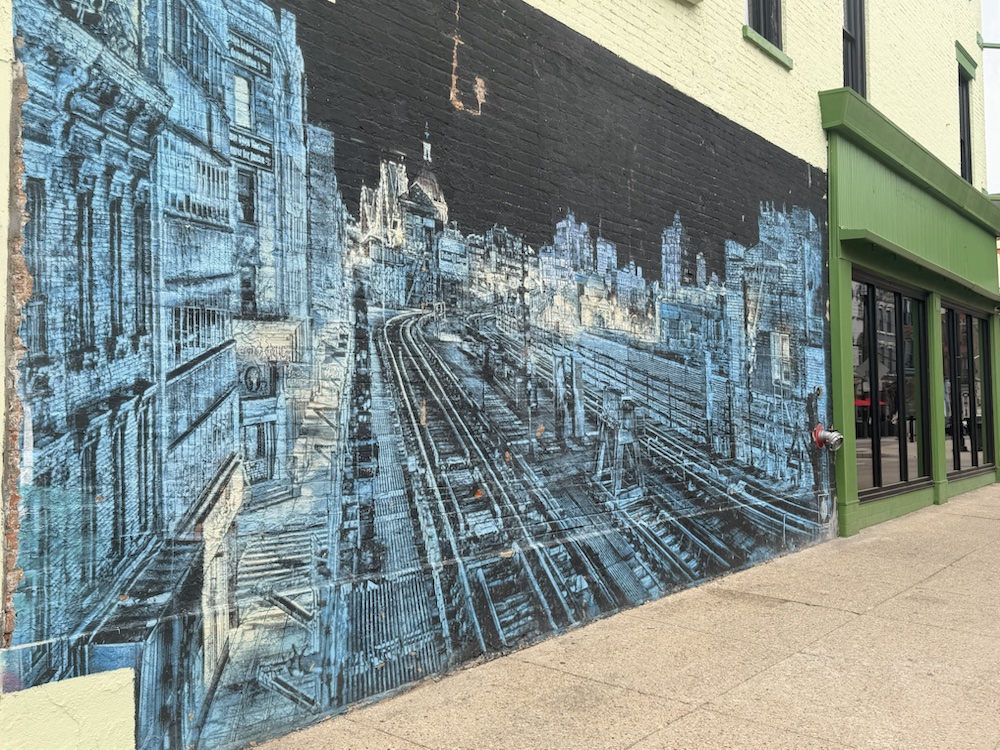 A blue mural with a city-and-track motif on a wall near Findlay Market.