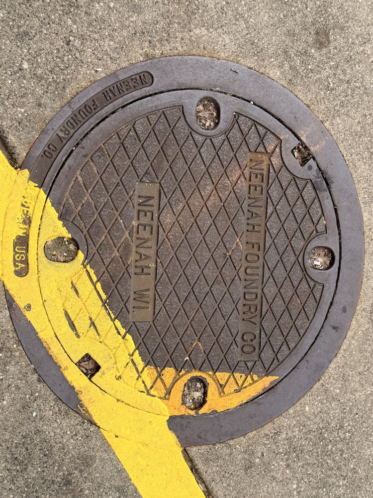 A round utility cover with yellow curb paint at Findlay Market.