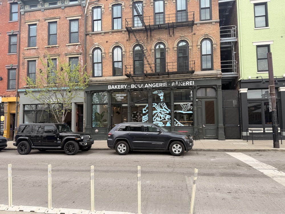 A bakery facade across the street from Findlay Market with brick upper stories and parked cars.