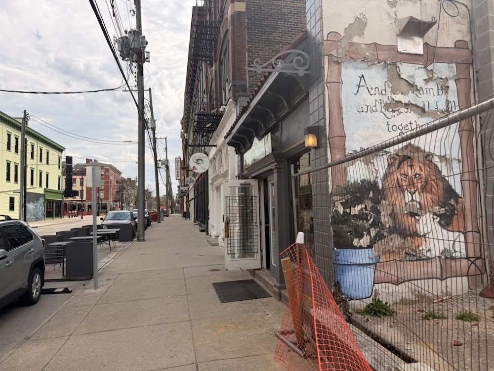 A lion mural painted on a weathered wall beside a sidewalk north of Findlay Market.